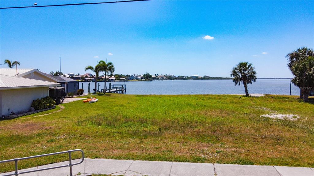 A grassy waterfront lot features a small dock, two kayaks, and palm trees under blue skies — 4456 HARBOR BOULEVARD, PORT CHARLOTTE, FL