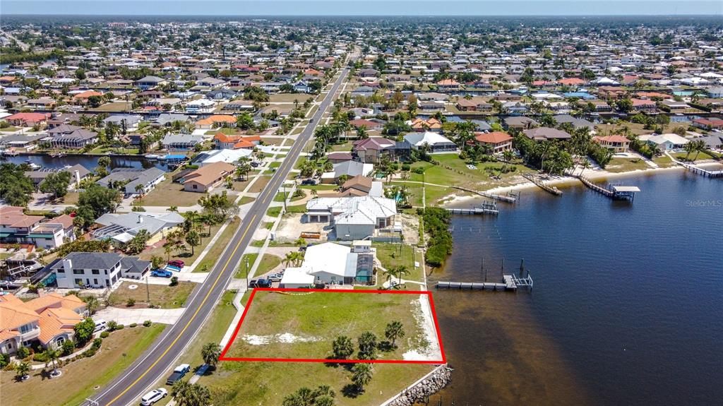 An aerial view shows a vacant waterfront lot outlined in red next to a road — 4456 HARBOR BOULEVARD, PORT CHARLOTTE, FL