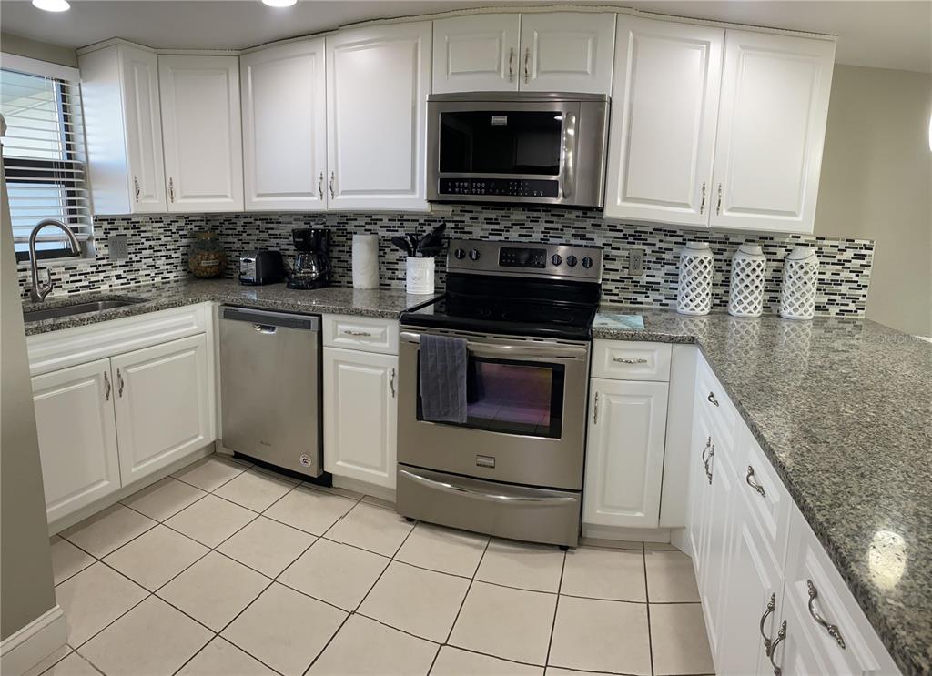 A kitchen features white cabinets, granite countertops, stainless steel appliances, and a mosaic tile backsplash — 1571 S ATLANTIC AVENUE UNIT 403, NEW SMYRNA BEACH, FL