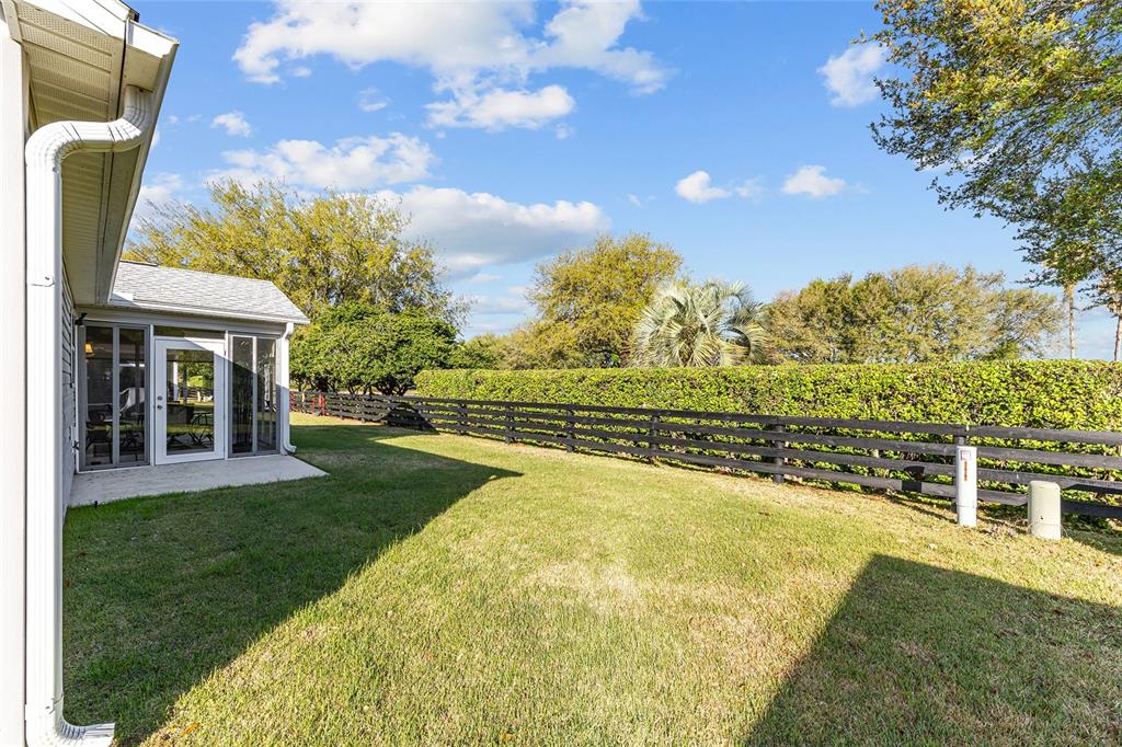 A grassy backyard features a screened-in patio, a black wooden fence, and mature trees — 1449 MURRELLS INLET LOOP, THE VILLAGES, FL