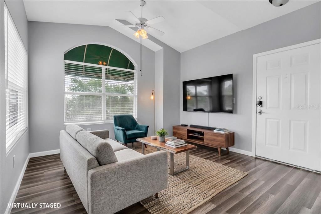 A living room with gray walls, wood-look flooring, a vaulted ceiling, and a large window — 10764 70TH AVENUE UNIT 3307, SEMINOLE, FL