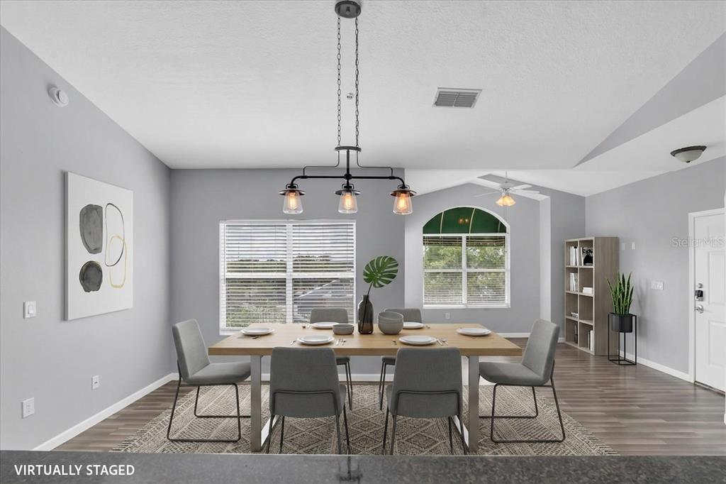 A virtually staged dining room with a wooden table, six gray chairs, and pendant lighting — 10764 70TH AVENUE UNIT 3307, SEMINOLE, FL