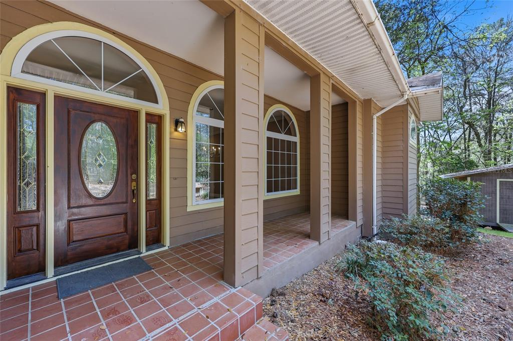 A covered front porch with tiled flooring leads to a wooden door with glass inserts — 19513 NW 240TH LANE, HIGH SPRINGS, FL