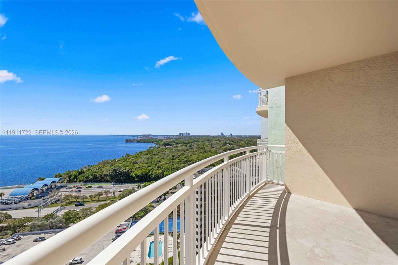 A balcony with a white railing overlooks a parking lot, trees, and the ocean — 2475 Brickell Ave # 1907, Miami FL 33129, MIAMI, FL