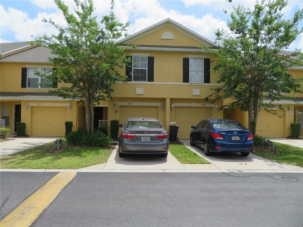 A row of yellow townhouses with attached garages and two cars parked in the driveways — 3387 CARUSO PLACE, OVIEDO, FL