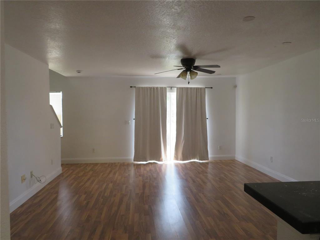 An empty living room features wood-look flooring, white walls, a ceiling fan, and sliding glass doors — 3387 CARUSO PLACE, OVIEDO, FL