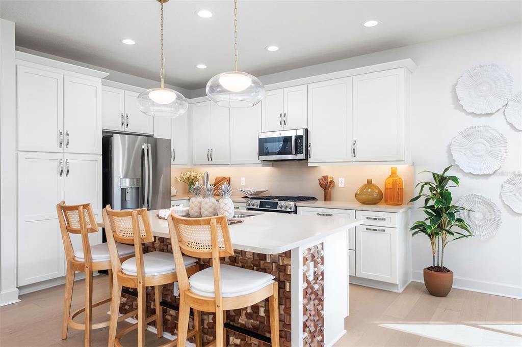 A modern kitchen features white cabinetry, a central island with bar seating, and stainless appliances — 3427 MALTA AVENUE, WESLEY CHAPEL, FL