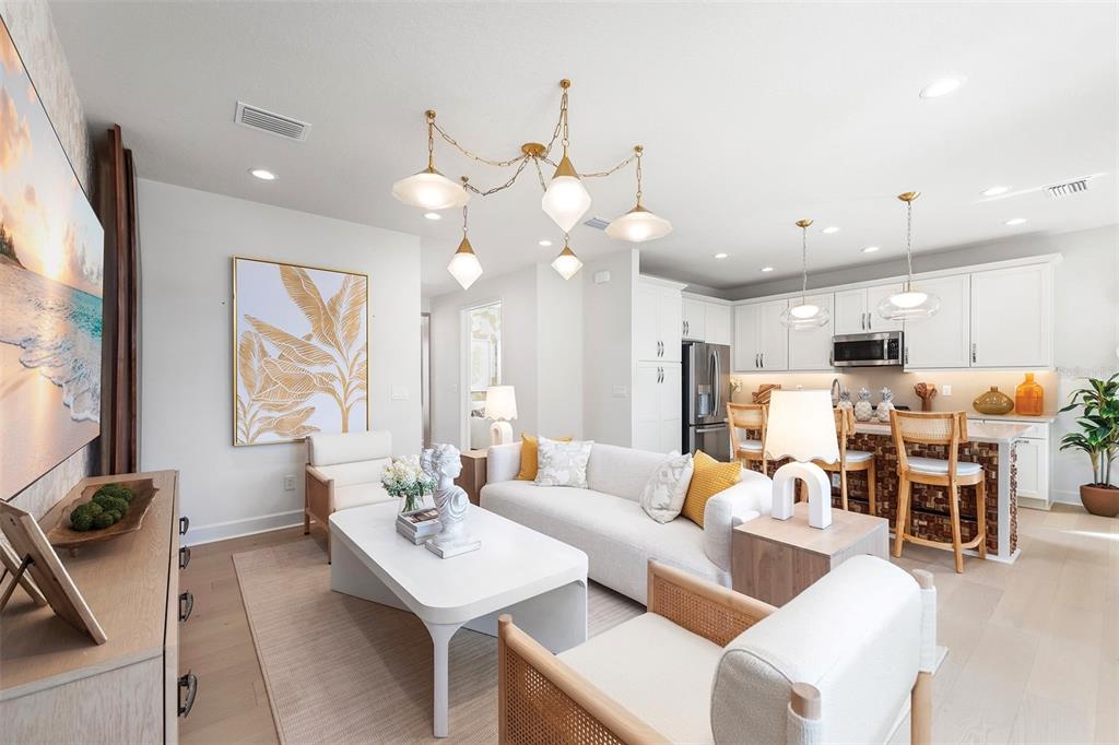 A bright living room features a white sofa, coffee table, and open kitchen with bar seating — 3427 MALTA AVENUE, WESLEY CHAPEL, FL