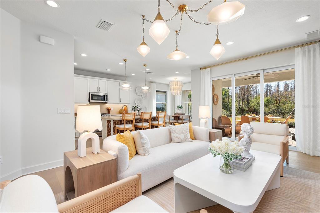 A bright open-concept living room and kitchen featuring white cabinetry, modern lighting, and sliding doors — 3427 MALTA AVENUE, WESLEY CHAPEL, FL