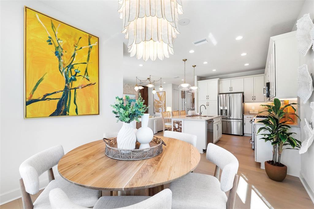 A dining area with a round wooden table and white chairs sits near a kitchen — 3427 MALTA AVENUE, WESLEY CHAPEL, FL