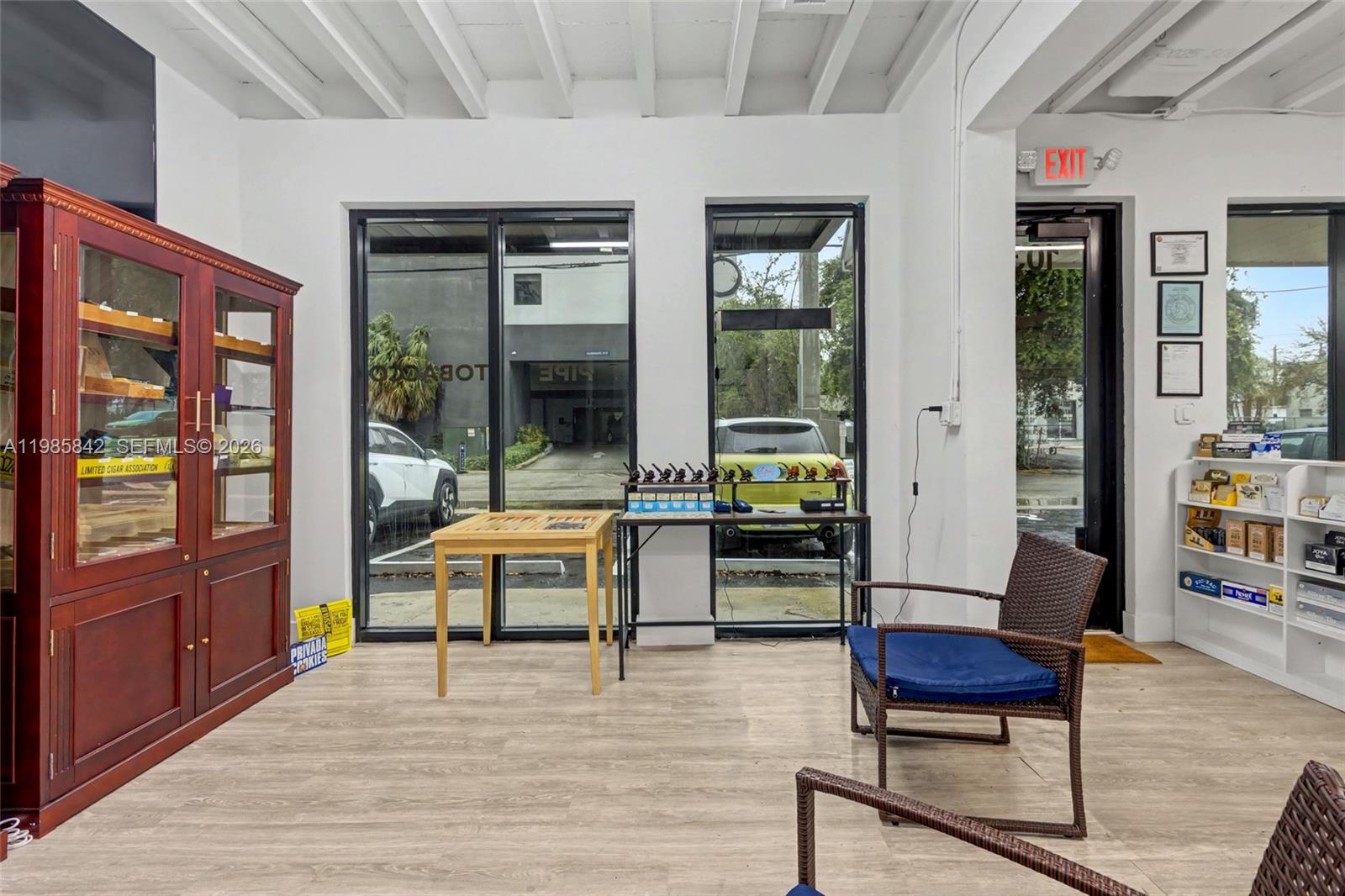 A retail shop interior features a wooden display cabinet, tables, chairs, and large glass windows — 24 NE 1st Ave, Dania Beach FL 33004, DANIA BEACH, FL