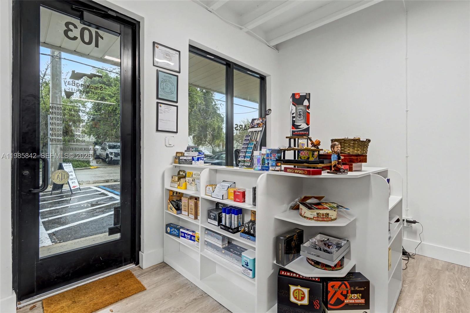 A retail shop interior features white shelving units stocked with various tobacco products and accessories — 24 NE 1st Ave, Dania Beach FL 33004, DANIA BEACH, FL