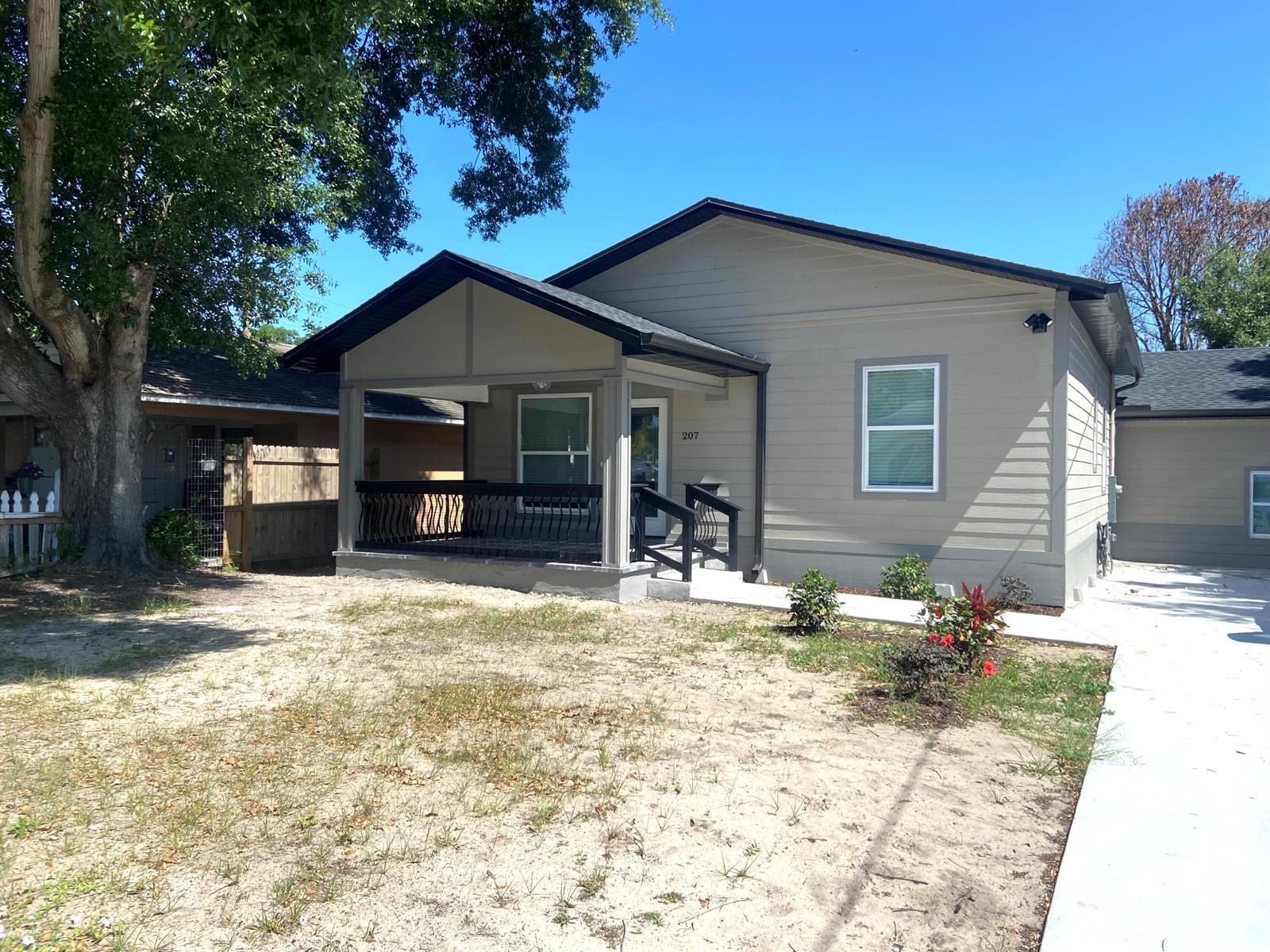 A single-story house with tan siding, a covered front porch, and a sandy front yard — 207 Ave E SE, Winter Haven FL 33880, WINTER HAVEN, FL