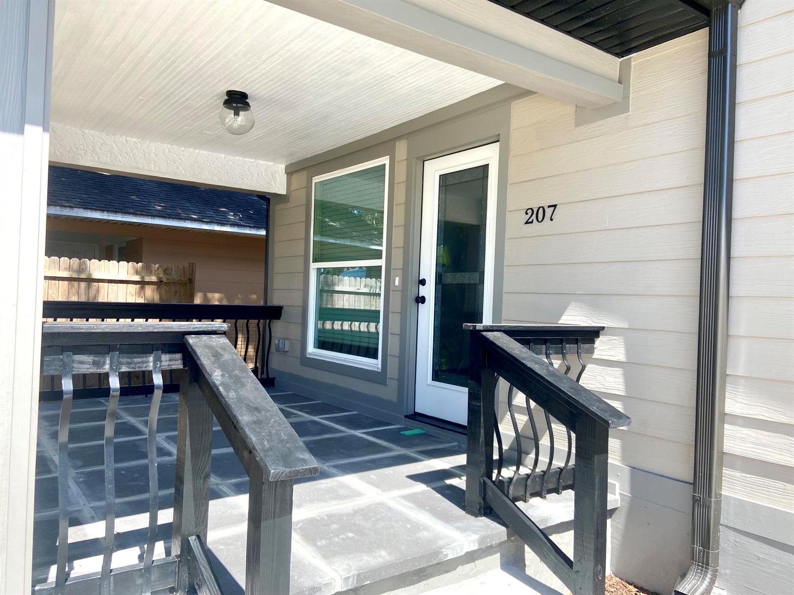 A covered porch features gray tiled flooring, black railings, and a white front door — 207 Ave E SE, Winter Haven FL 33880, WINTER HAVEN, FL