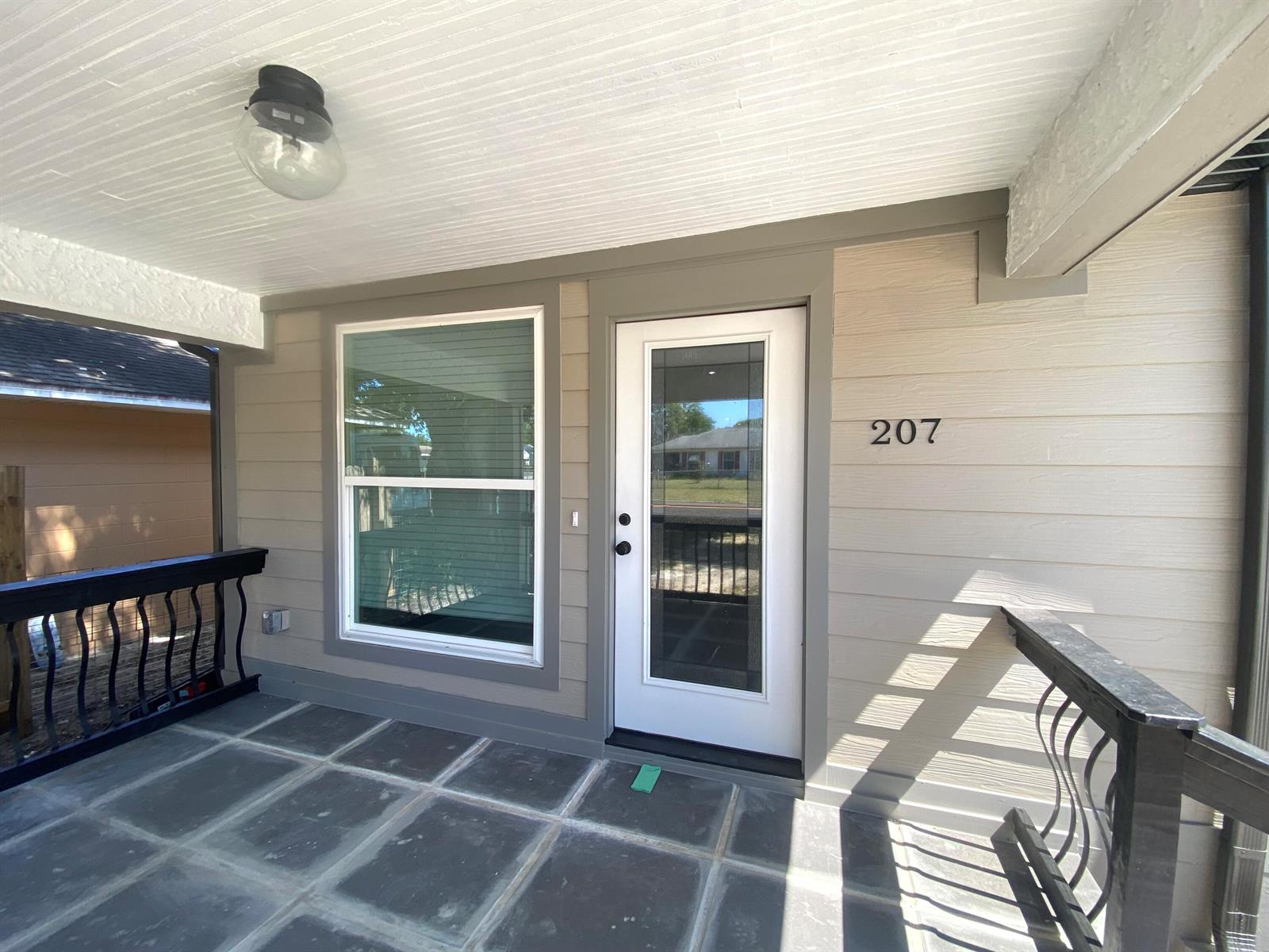 A covered porch features dark tiled flooring, a white front door, and black railings — 207 Ave E SE, Winter Haven FL 33880, WINTER HAVEN, FL