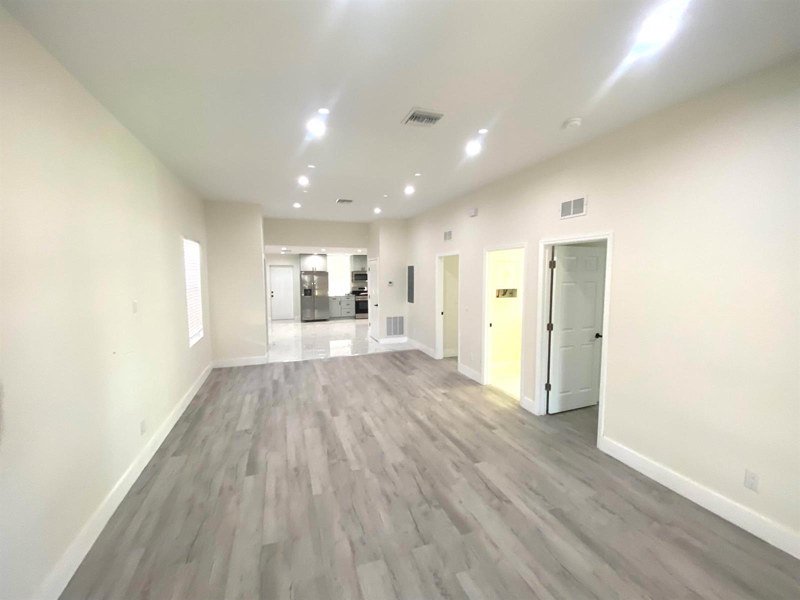 An open-concept living area features light-colored walls, gray wood-look flooring, and a distant kitchen — 207 Ave E SE, Winter Haven FL 33880, WINTER HAVEN, FL