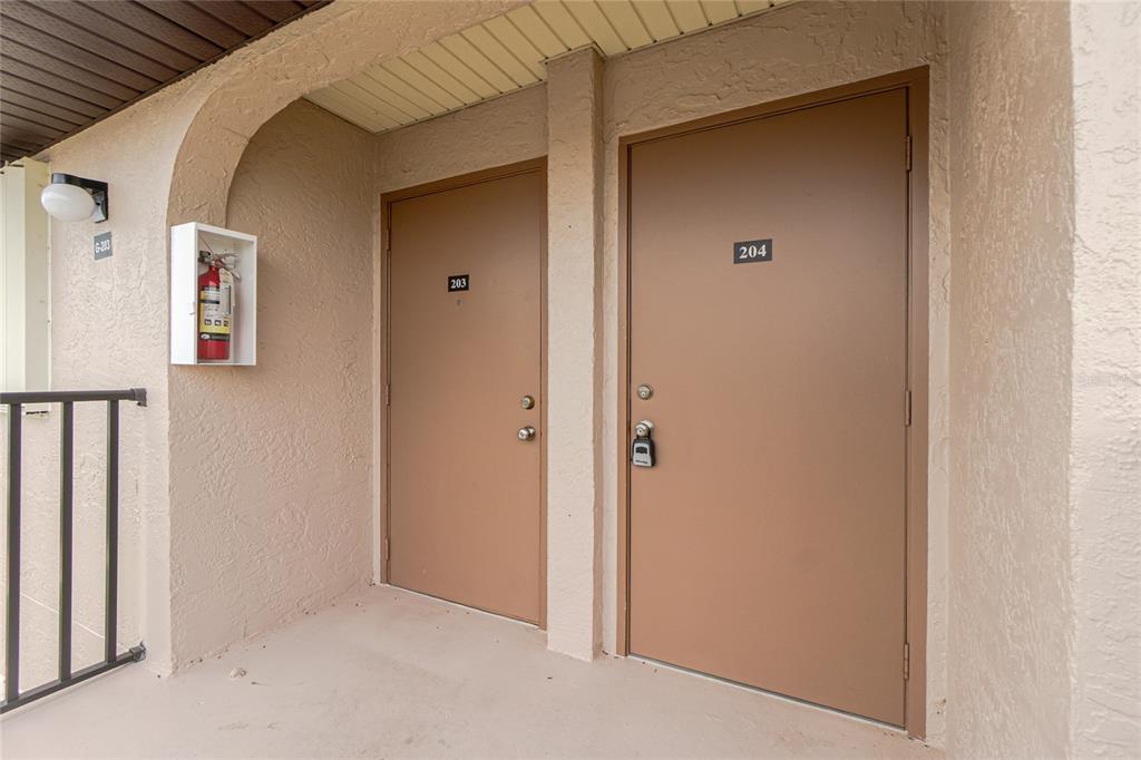 Two brown apartment doors labeled 203 and 204 are located on an outdoor walkway — 25100 SANDHILL BOULEVARD UNIT G204, PUNTA GORDA, FL