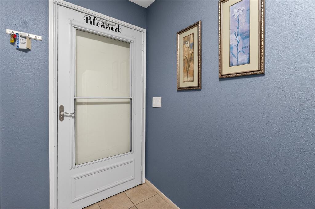 A white storm door with a "Blessed" sign opens into an entryway with blue walls — 25100 SANDHILL BOULEVARD UNIT G204, PUNTA GORDA, FL