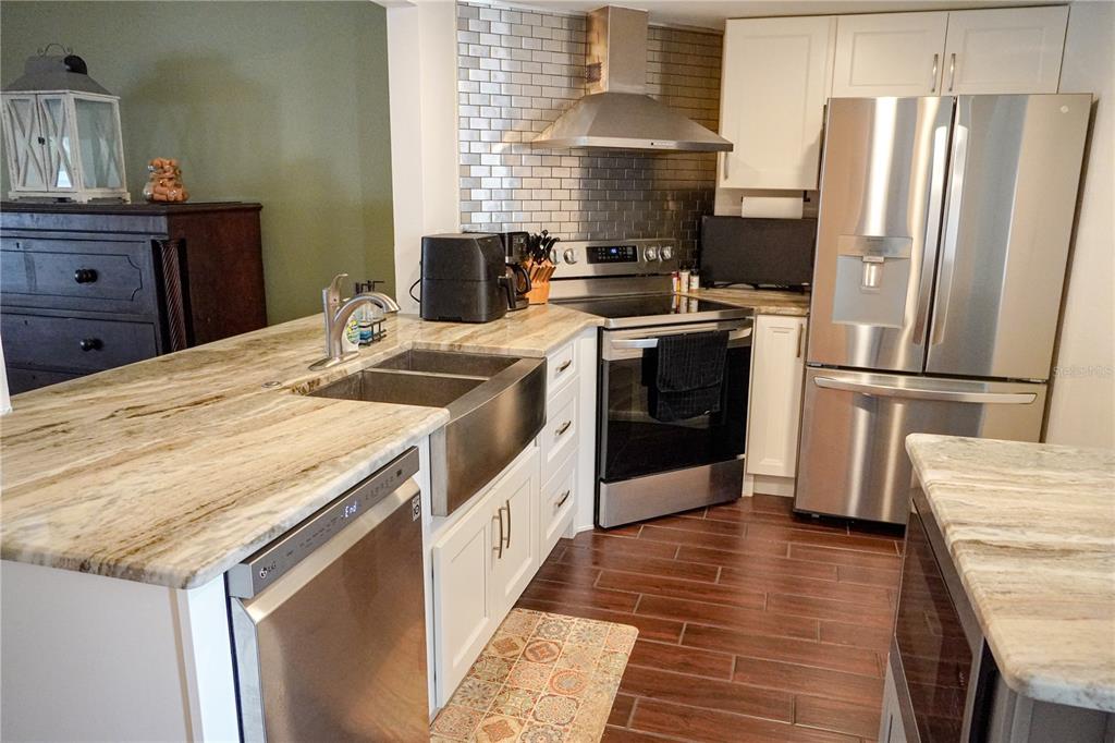 A kitchen features white cabinets, stainless steel appliances, a farmhouse sink, and granite countertops — 1963 GEORGIA CIRCLE N, CLEARWATER, FL