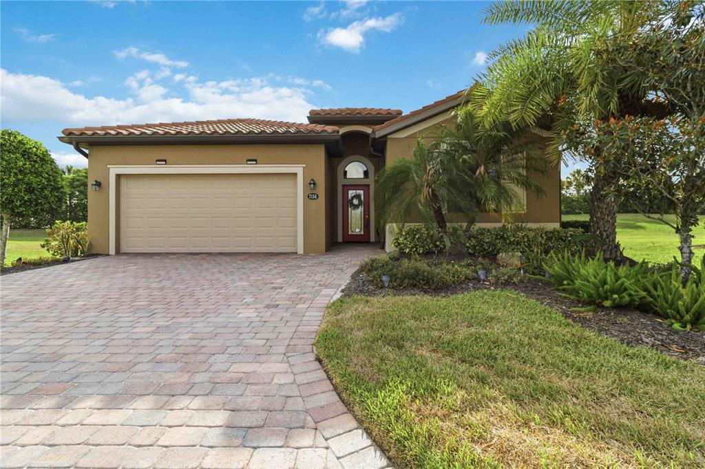 A single-story house with a tan stucco exterior, tile roof, and a paved driveway — 7156 MARSH VIEW TERRACE, BRADENTON, FL