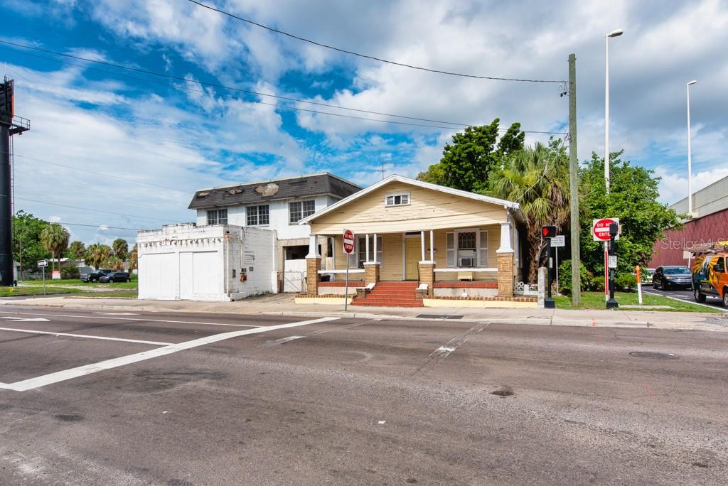A yellow bungalow with a front porch sits next to a white industrial building — 1406 N HOWARD AVENUE, TAMPA, FL