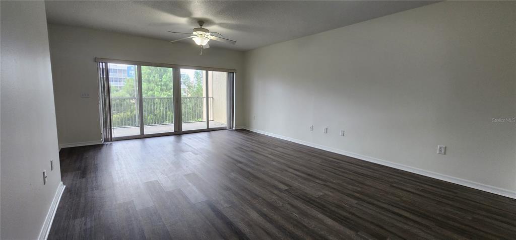 An empty living room features dark wood-look flooring, a ceiling fan, and sliding glass balcony doors — 960 STARKEY UNIT 3302, LARGO, FL