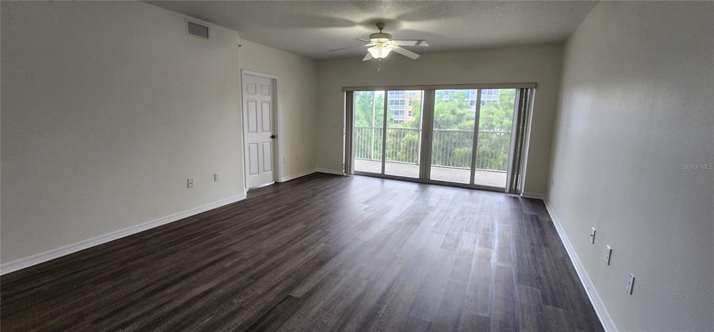 An empty room features dark wood-look flooring, a ceiling fan, and sliding glass balcony doors — 960 STARKEY UNIT 3302, LARGO, FL