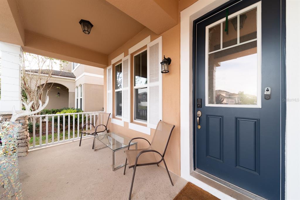 A covered front porch features a dark blue door, two chairs, and a glass table — 2542 NOUVEAU WAY, KISSIMMEE, FL