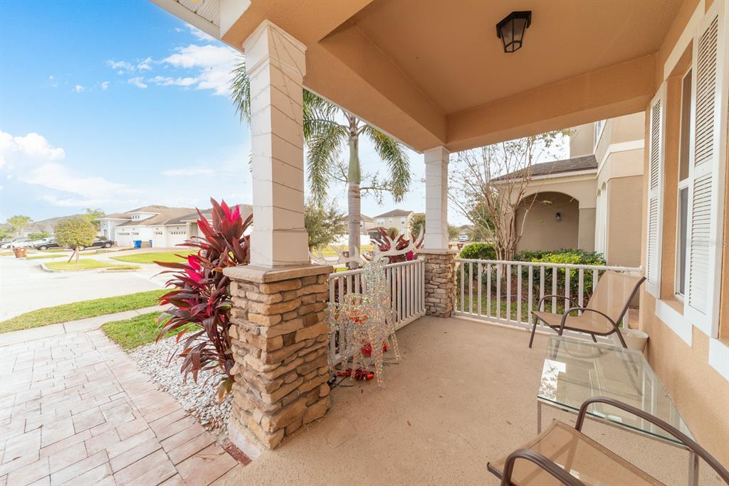 A covered front porch features stone-based columns, a white railing, and outdoor furniture — 2542 NOUVEAU WAY, KISSIMMEE, FL