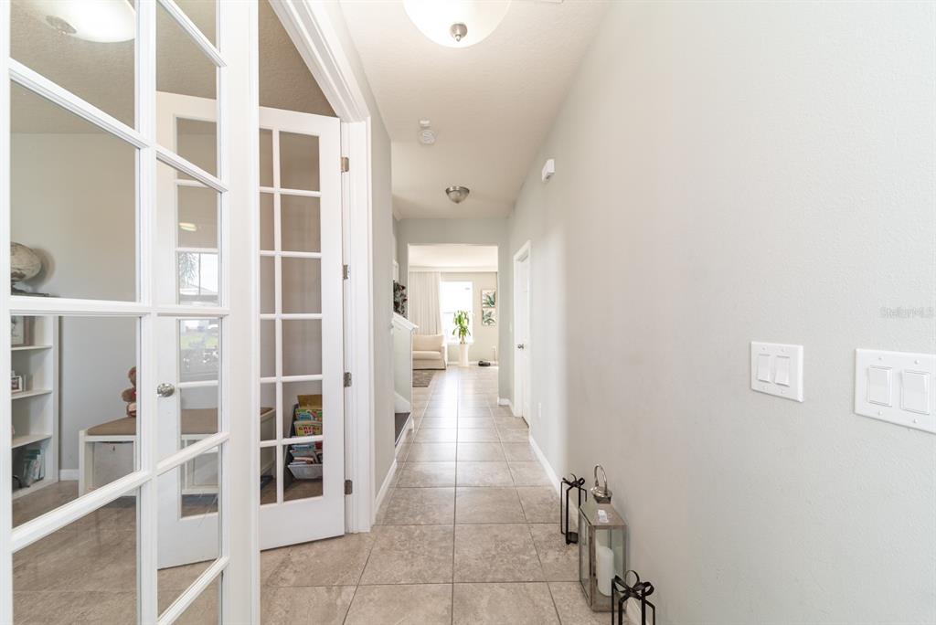 A tiled hallway leads past glass-paneled French doors toward a bright room in the distance — 2542 NOUVEAU WAY, KISSIMMEE, FL