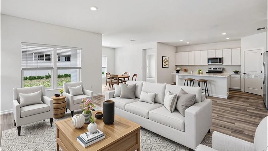 This open-concept living room features a white sofa, two armchairs, and a kitchen with island — 24258 NW 13TH BOULEVARD, NEWBERRY, FL