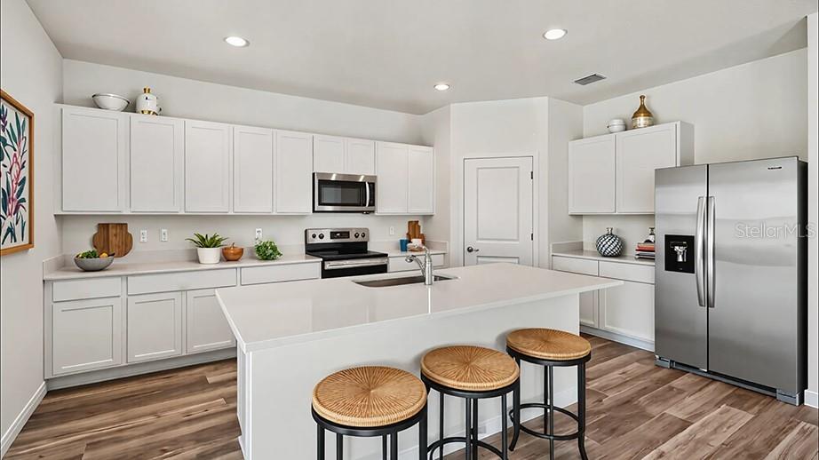 A modern kitchen features white cabinetry, a central island with bar stools, and stainless steel appliances — 24258 NW 13TH BOULEVARD, NEWBERRY, FL