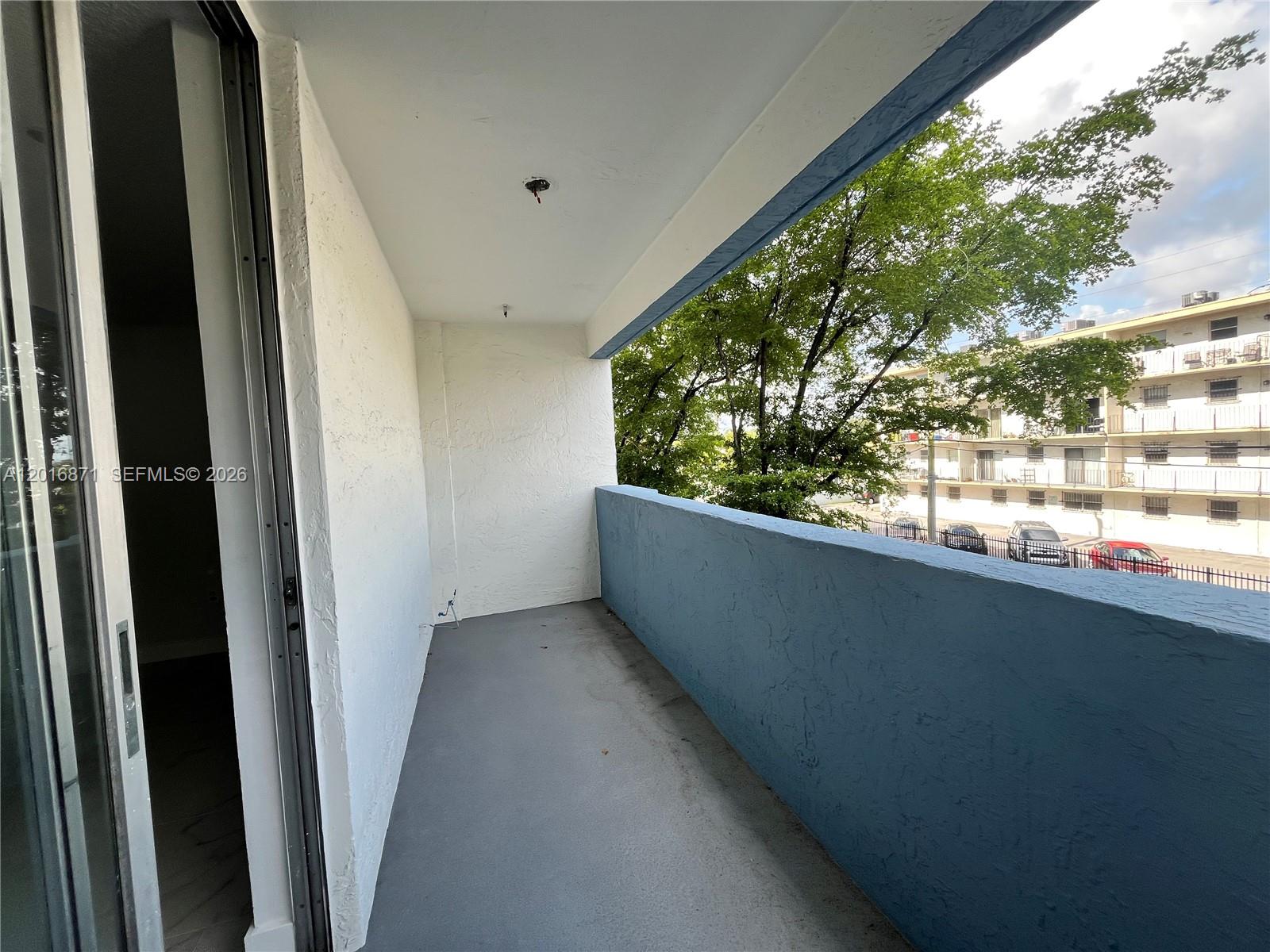 A balcony with a gray floor, white walls, and a blue railing overlooks a parking lot — 5050 NW 7th St # 220, Miami FL 33126, MIAMI, FL