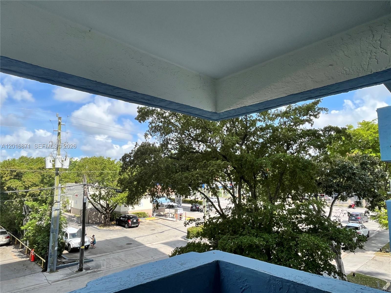 A view from a balcony overlooks a parking lot, trees, and a street — 5050 NW 7th St # 220, Miami FL 33126, MIAMI, FL