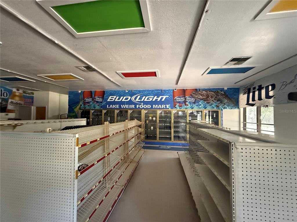 An empty retail store interior features metal shelving units and a Bud Light wall mural — 3380 SE LAKE WEIR AVENUE UNIT A, OCALA, FL
