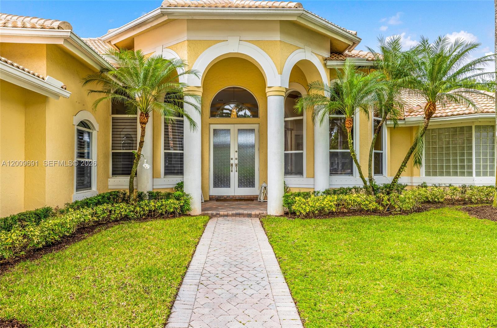 The exterior of a yellow house features a stone walkway leading to a double-door entrance — 2477 Poinciana Dr, Weston FL 33327, WESTON, FL