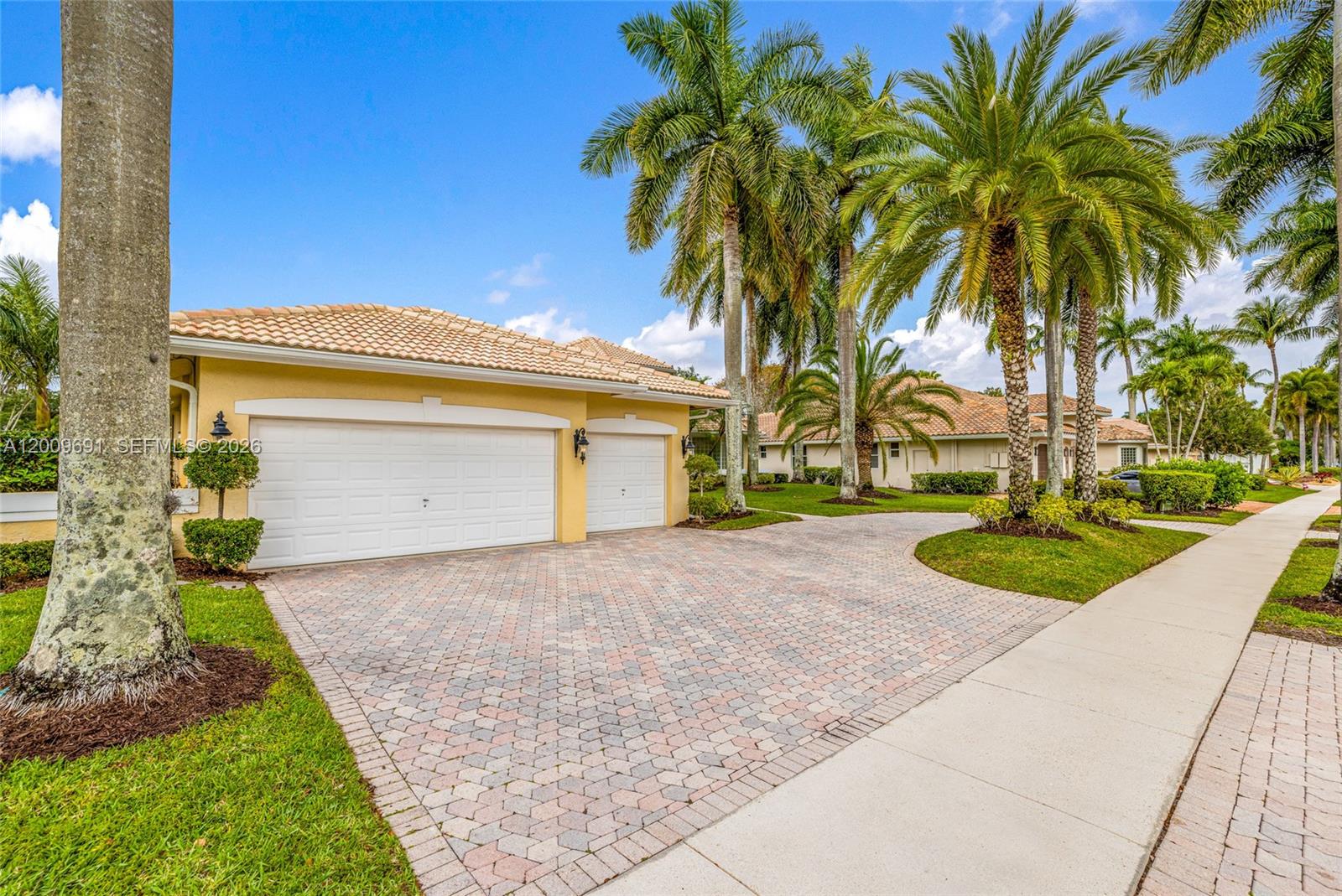 A yellow house with a two-car garage and a paved driveway sits under palm trees — 2477 Poinciana Dr, Weston FL 33327, WESTON, FL