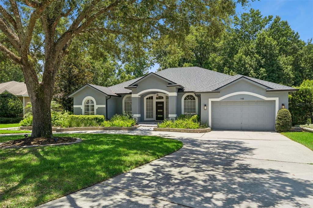 A single-story gray house with a two-car garage and a large tree in the yard — 148 WISTERIA DRIVE, LONGWOOD, FL