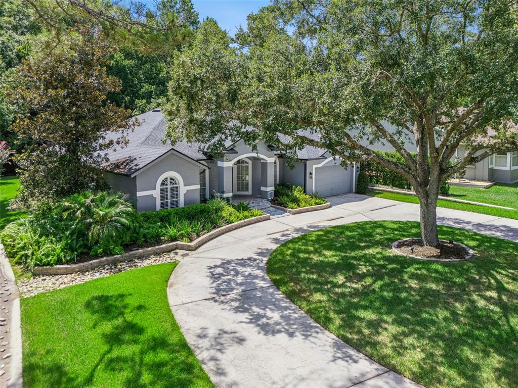 An aerial view of a gray single-story house with a curved driveway and large trees — 148 WISTERIA DRIVE, LONGWOOD, FL