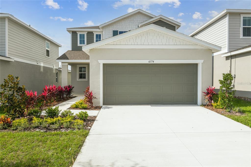 A two-story house with a beige stucco facade, a gray garage door, and landscaped front yard — 6174 DAPHNE STREET, LAKE HAMILTON, FL