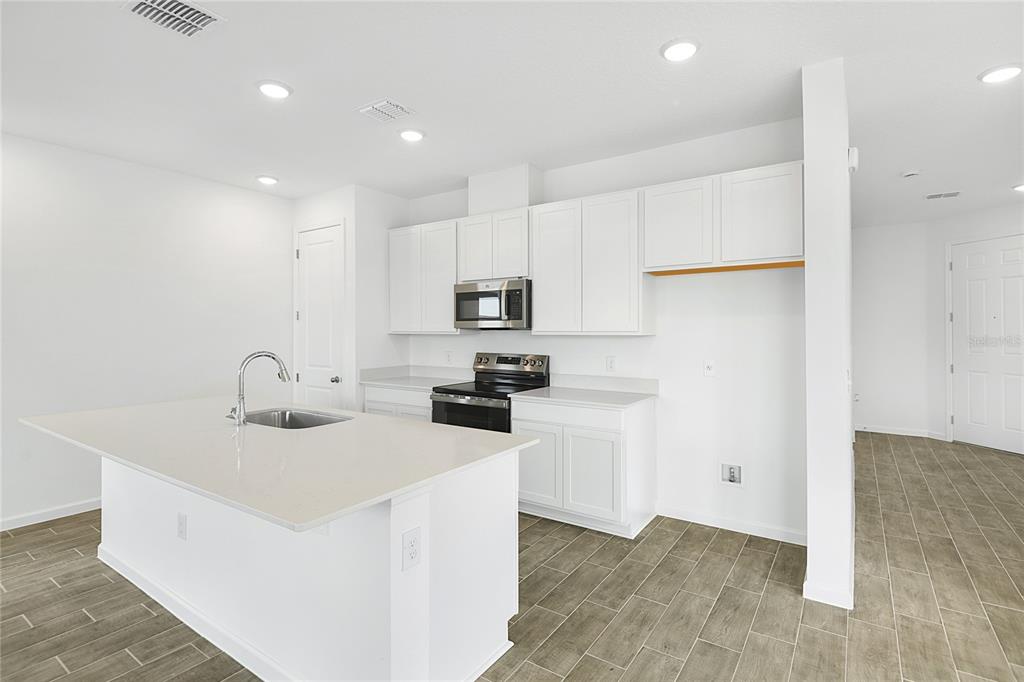 A modern kitchen features white cabinets, a central island with a sink, and tile flooring — 6174 DAPHNE STREET, LAKE HAMILTON, FL