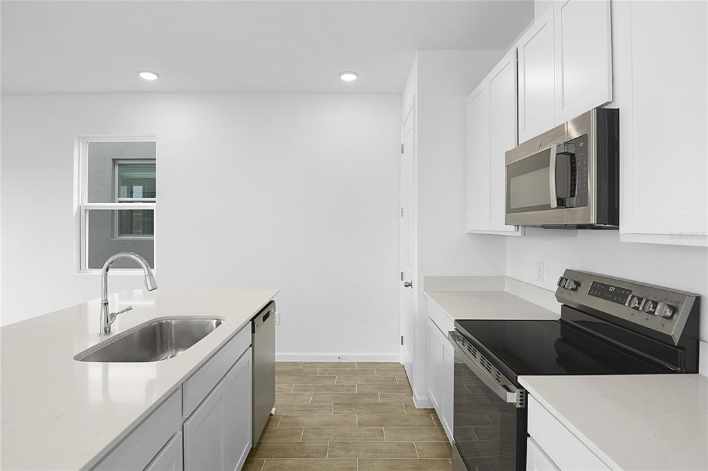 A modern kitchen features white cabinets, stainless steel appliances, a quartz island, and tile flooring — 6174 DAPHNE STREET, LAKE HAMILTON, FL