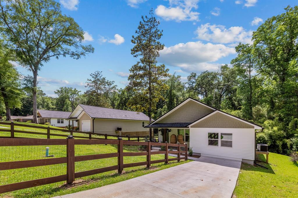 A white house with a green gable and a concrete driveway sits behind a wooden fence — 618 N STEWART STREET, QUINCY, FL