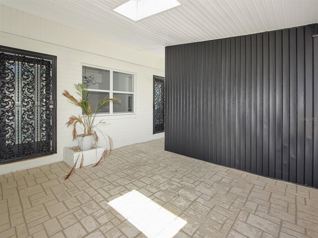 A covered patio features a tiled floor, white brick walls, and a dark vertical-paneled wall — 342 BOYLSTON AVENUE, DAYTONA BEACH, FL