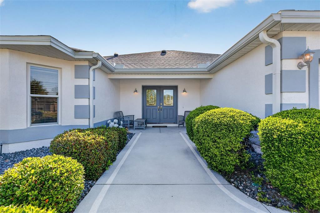 A concrete walkway leads to the double front doors of a house with stucco siding — 3183 KEARNS CORNER, THE VILLAGES, FL