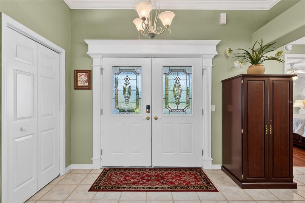 An entryway features double glass-paneled doors, a red rug, and a tall wooden cabinet — 3183 KEARNS CORNER, THE VILLAGES, FL