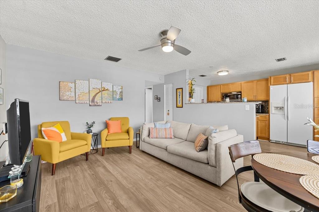 A living room with light wood flooring, a beige sofa, and two yellow armchairs — 1235 S HIGHLAND AVENUE UNIT 2-307, CLEARWATER, FL