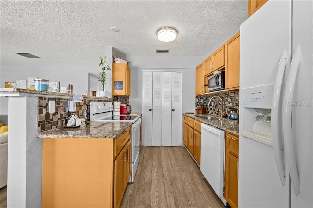 A kitchen features light wood cabinets, granite countertops, a tiled backsplash, and white appliances — 1235 S HIGHLAND AVENUE UNIT 2-307, CLEARWATER, FL