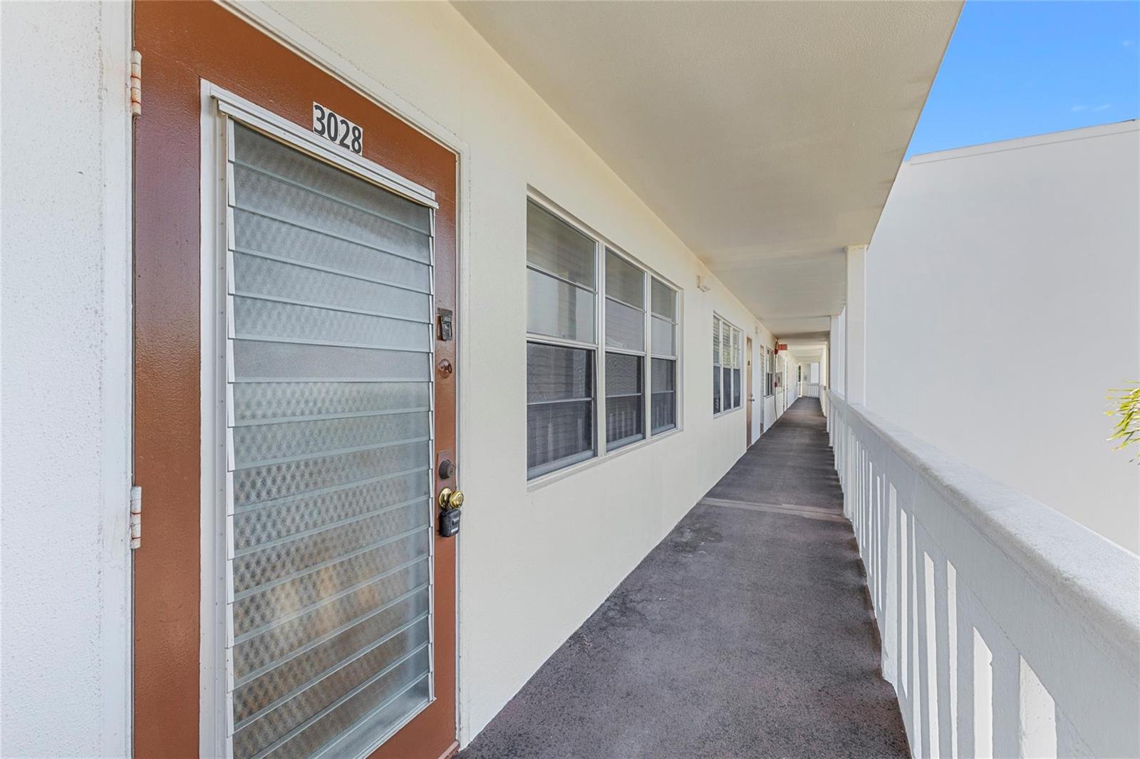 An exterior walkway with a brown door numbered 3028 and windows along a white building — 3028 Newport H, Deerfield Beach FL 33442, DEERFIELD BEACH, FL