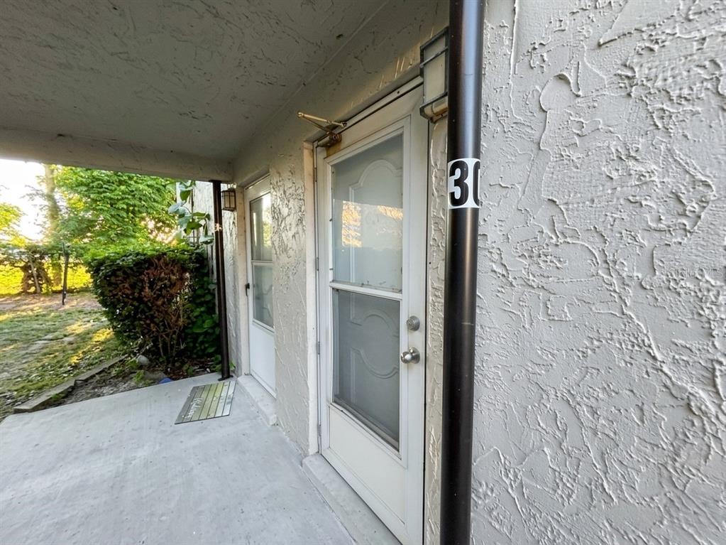 A concrete walkway leads to two white exterior doors with storm doors under a porch — 1103 CYPRESS GARDENS BOULEVARD UNIT 30, WINTER HAVEN, FL